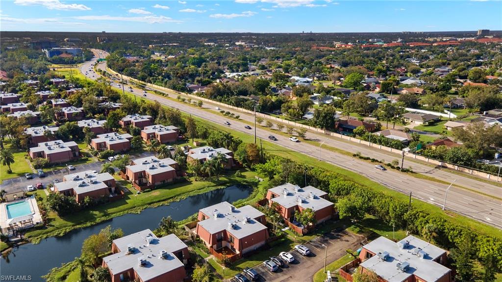 Aerial perspective showcasing a residential development with multiple units, featuring a community swimming pool, an adjacent pond, and mature landscaping
