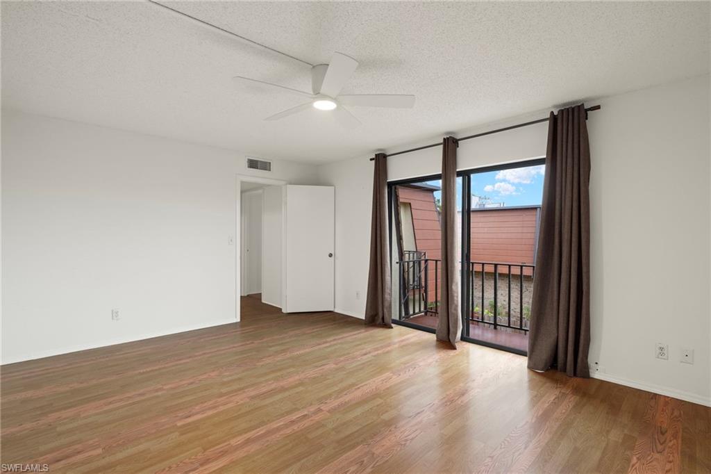 Bright room featuring wood-finish flooring, a white ceiling fan with integrated lighting, and a private balcony accessed through sliding glass doors