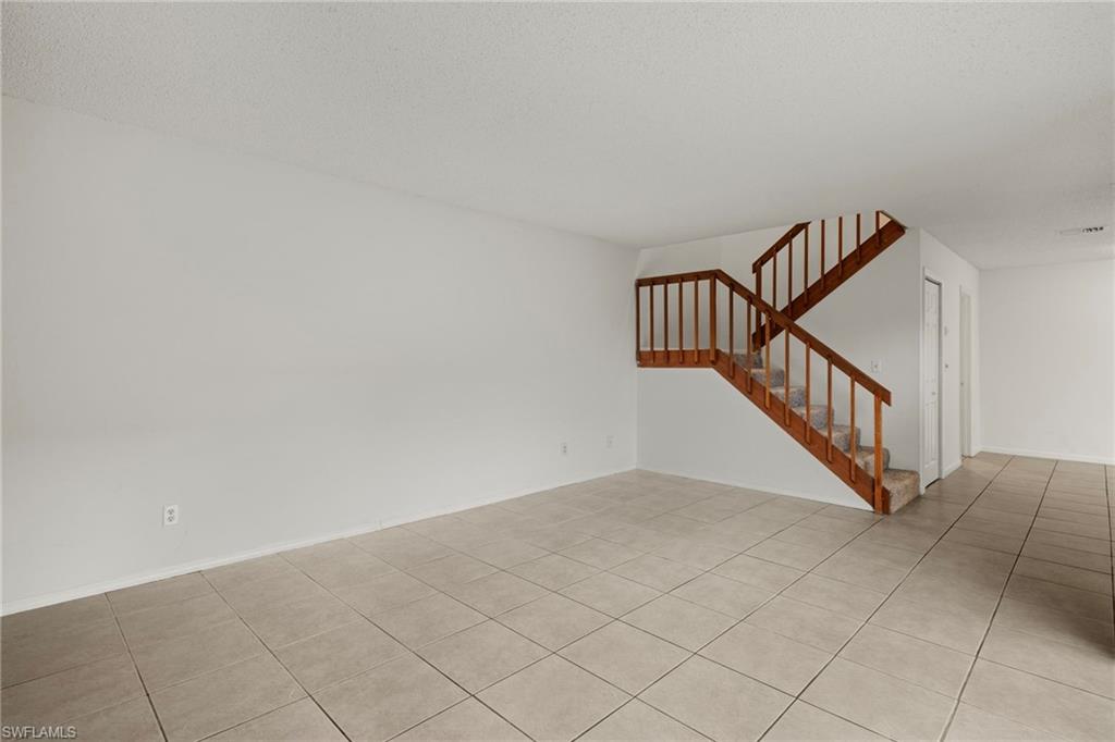 Spacious room featuring neutral tile flooring and a carpeted staircase with wood-finish railings