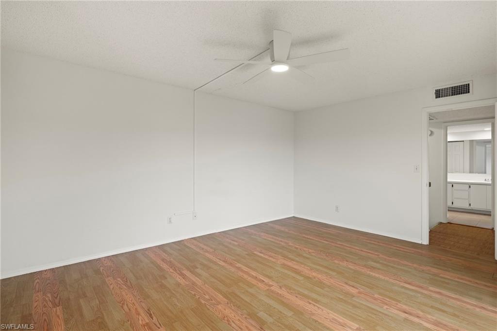 Spacious room featuring wood-finish flooring, white walls, and a ceiling fan
