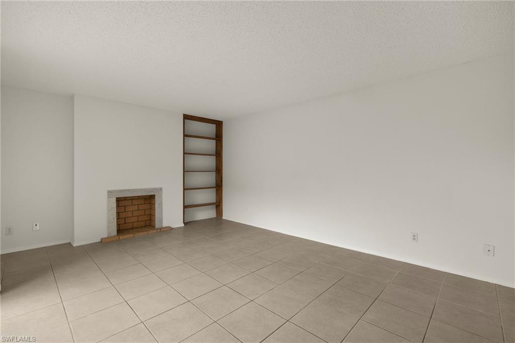 Living area featuring a brick fireplace with a stone hearth, built-in wooden shelving, and square tile flooring