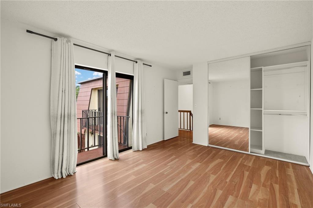 Spacious room featuring wood-finish flooring and a full-wall mirrored closet with built-in shelving and hanging rods