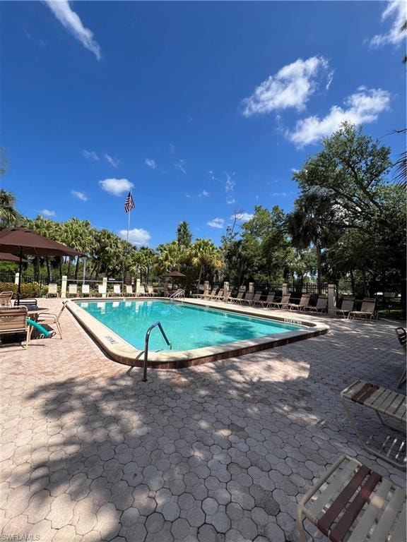 Community swimming pool featuring a paver deck surround, ample lounge seating, and mature tropical landscaping