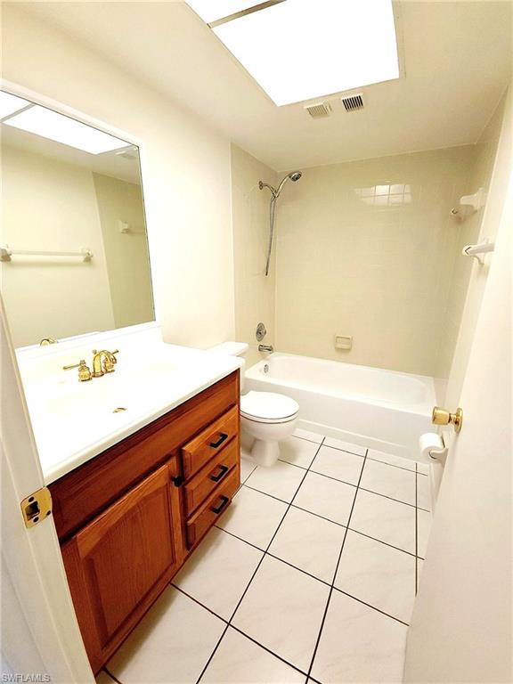 Bathroom featuring a wood-finish vanity with a white countertop, a white toilet, and a white tub with shower