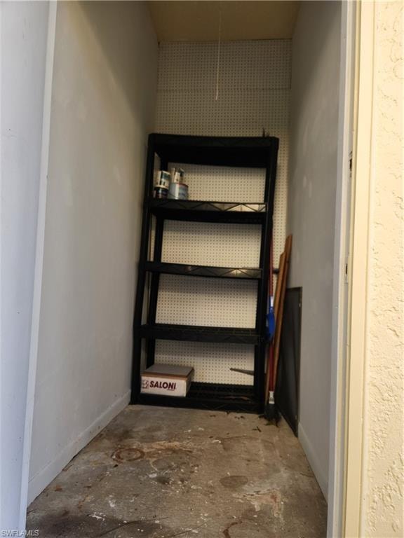 Enclosed storage area featuring concrete flooring and white pegboard wall panels