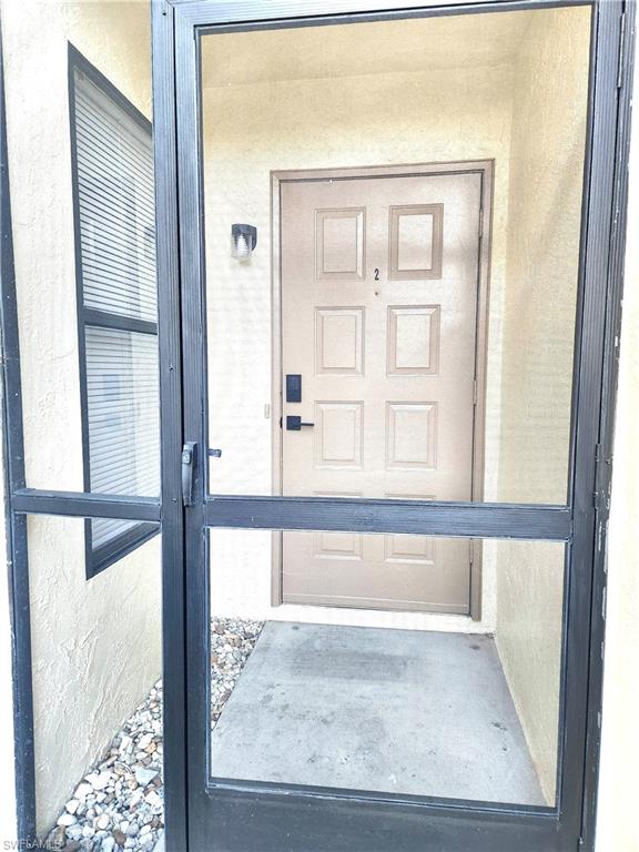 Entryway featuring a four-panel main door with contemporary hardware, a black-framed screen door, and an exterior wall sconce