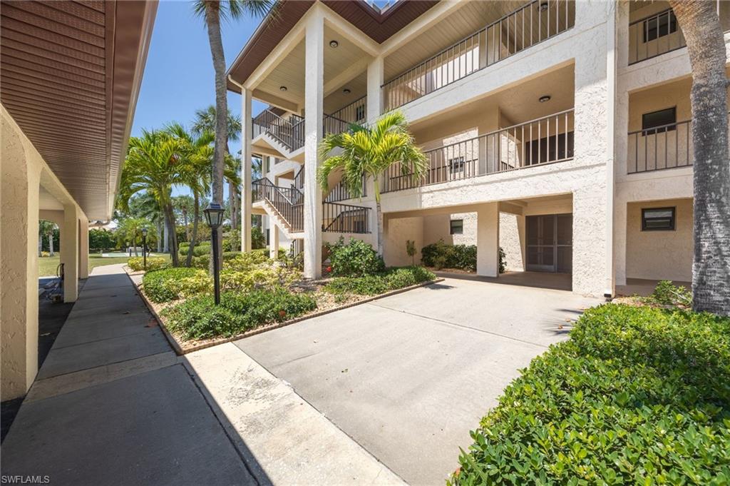 Multi-story stucco exterior featuring balconies with black metal railings, a covered walkway, and mature tropical landscaping