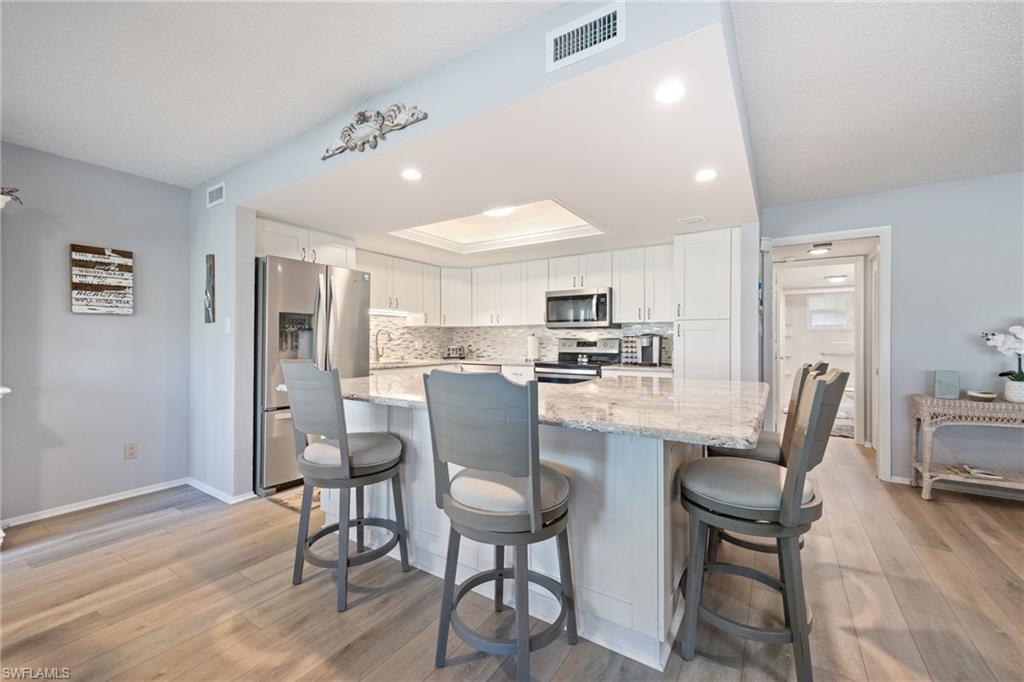 Kitchen featuring a peninsula with counter seating, a stone countertop, a tile backsplash, stainless steel appliances, and wood-finish flooring