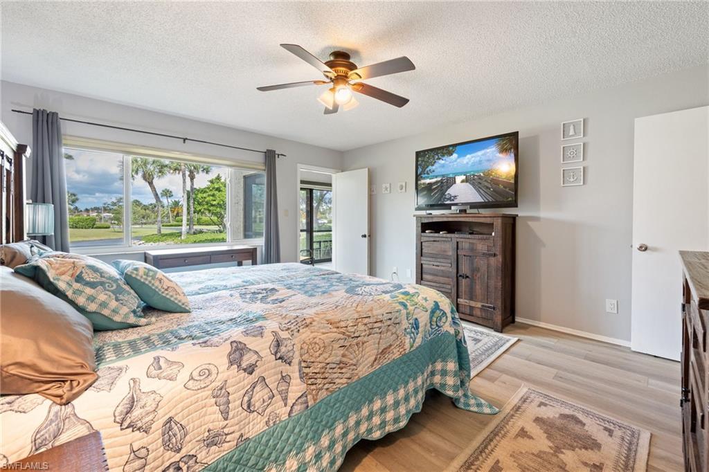 Bedroom featuring wood-finish flooring, a ceiling fan with integrated lighting, and a wide window offering exterior landscaping