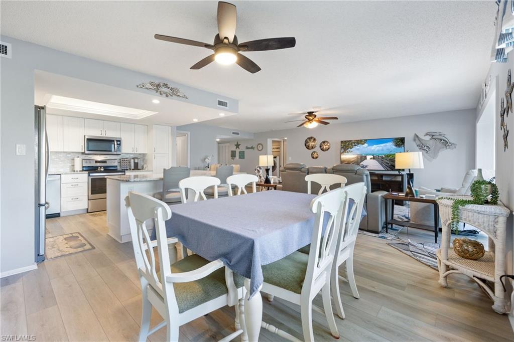 Open-concept living area featuring wood-finish flooring throughout, a kitchen with white cabinetry and stainless steel appliances, and ceiling fans