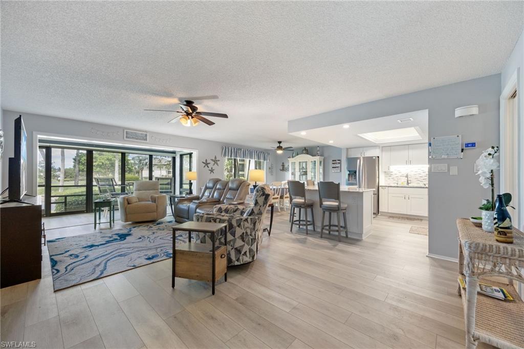 Light wood-finish flooring extends through an open-concept living area with a ceiling fan