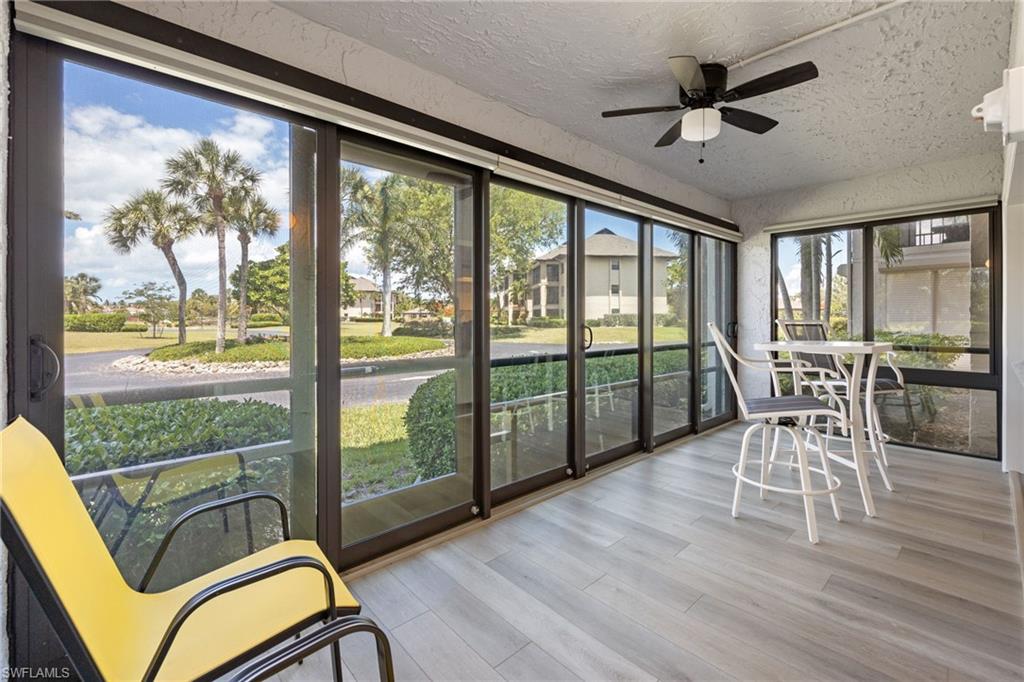 Enclosed patio featuring floor-to-ceiling sliding glass doors, light wood-finish flooring, and a ceiling fan with integrated lighting