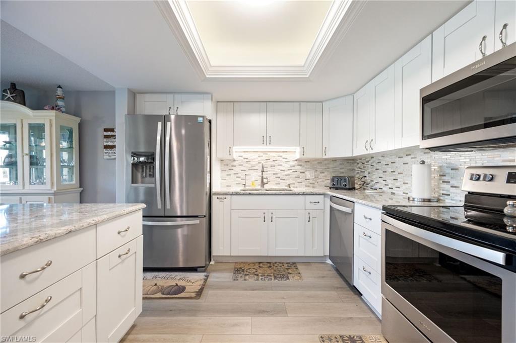 Kitchen featuring white shaker-style cabinetry, stainless steel appliances, light-toned granite countertops, and a mosaic tile backsplash
