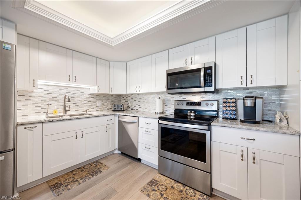 Kitchen featuring white shaker-style cabinetry, stainless steel appliances, light-toned countertops, a glass tile backsplash, and wood-finish flooring