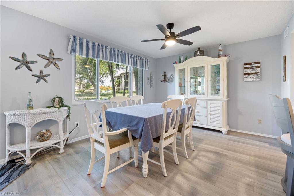 Dining area featuring light-toned wood-finish flooring, a contemporary ceiling fan with integrated lighting, and multiple windows providing ample natural light