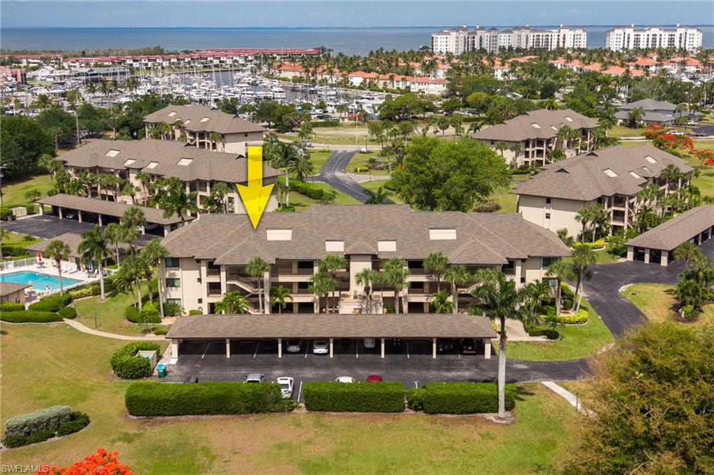 Multi-story condominium building featuring carports, an exterior staircase, and mature palm landscaping