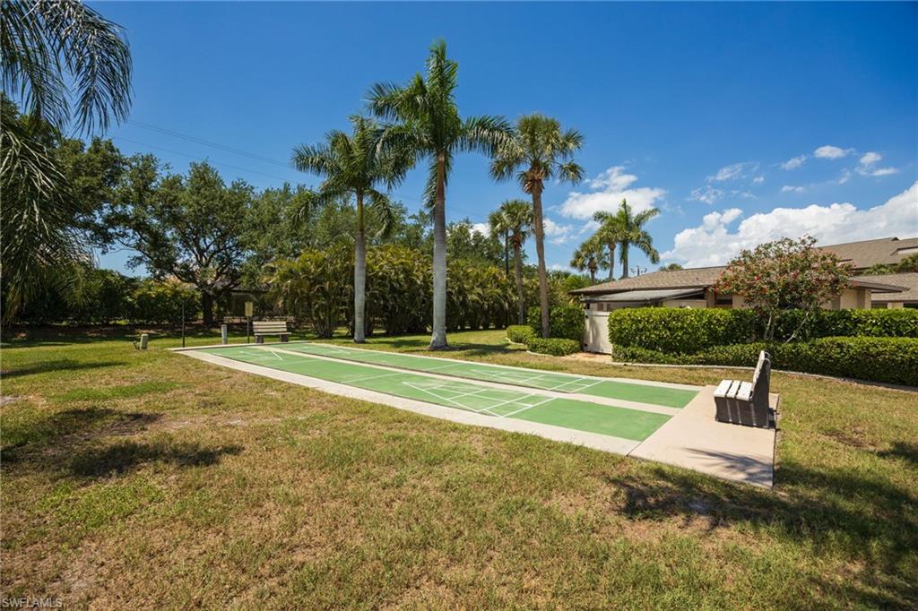 Outdoor shuffleboard court featuring a green playing surface with white markings, surrounded by manicured grass
