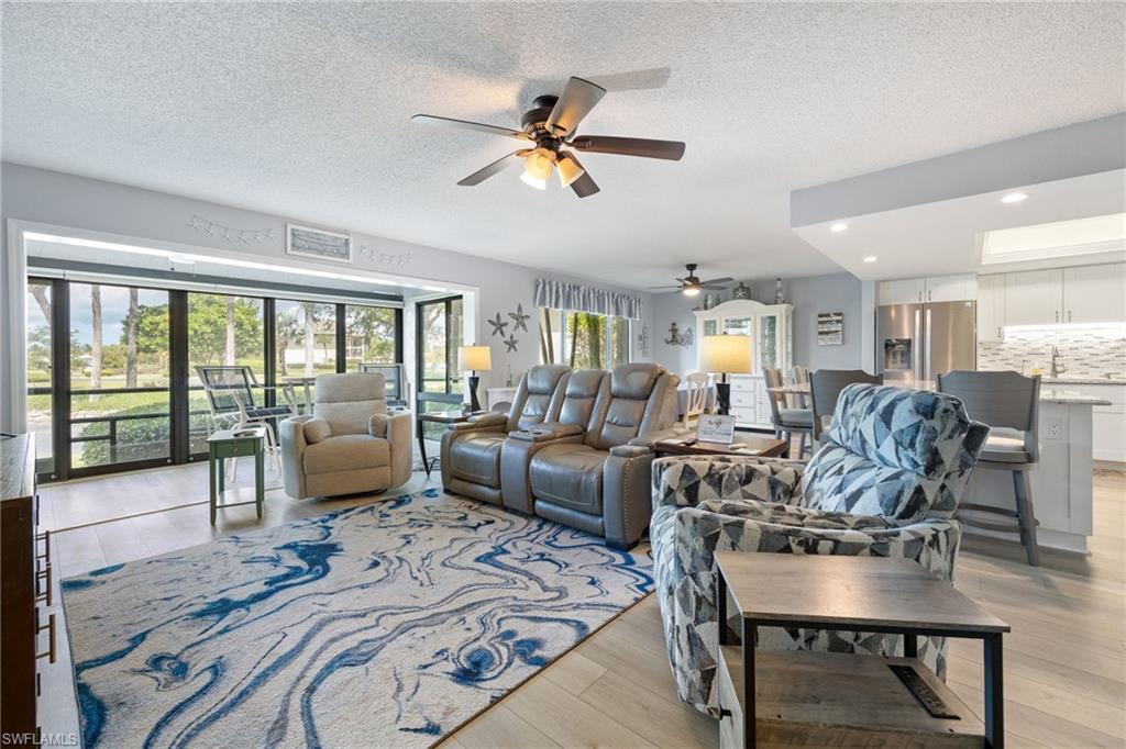 Spacious open-concept living area featuring light wood-finish flooring, a large area rug, and a ceiling fan