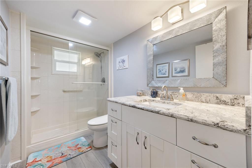 Bathroom featuring a frameless glass shower enclosure, a window, and a white vanity with a granite countertop and an undermount sink