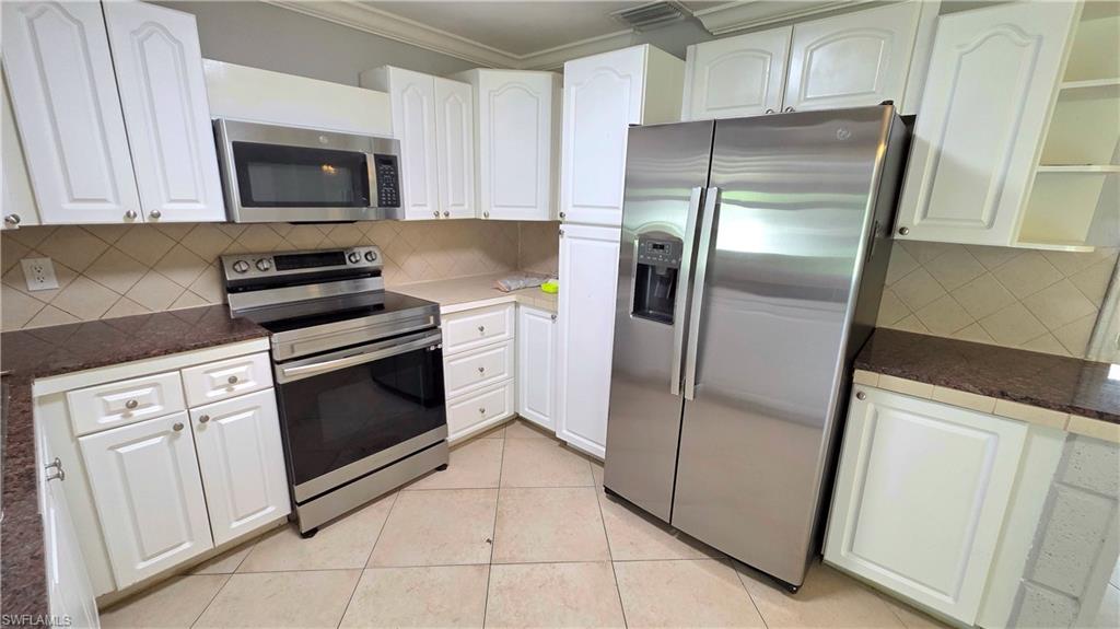 Kitchen featuring stainless steel appliances, white cabinetry, brown countertops, and diagonal tile backsplash