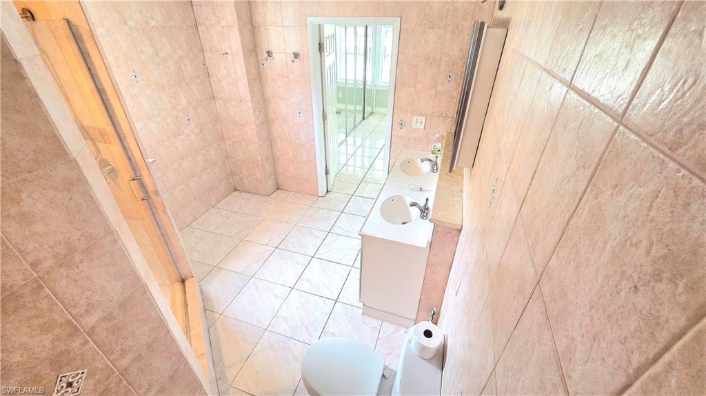 Tile flooring throughout featuring a dual vanity with undermount sinks, a toilet, and a glass-enclosed shower