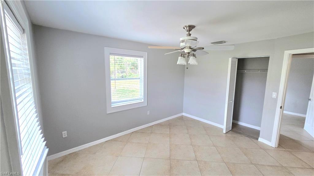 Bedroom #3  featuring light gray walls, tile flooring, a window with horizontal blinds, a ceiling fan with integrated lighting, and an open closet with shelving