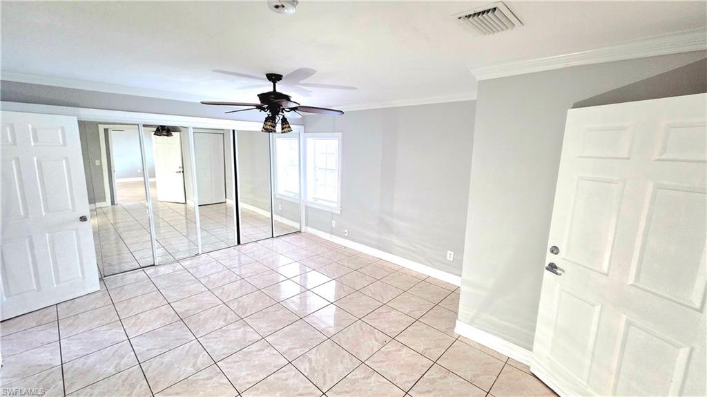 Spacious room featuring light-colored tile flooring, full-wall mirrored closet doors, a ceiling fan with integrated lighting, and two windows providing natural light