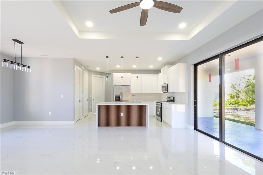 Kitchen featuring white cabinets, hanging light fixtures, a center island, stainless steel appliances, and a raised ceiling