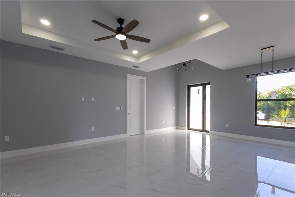 Empty room featuring light marble finish floors, a tray ceiling, ceiling fan, recessed lighting, and a chandelier