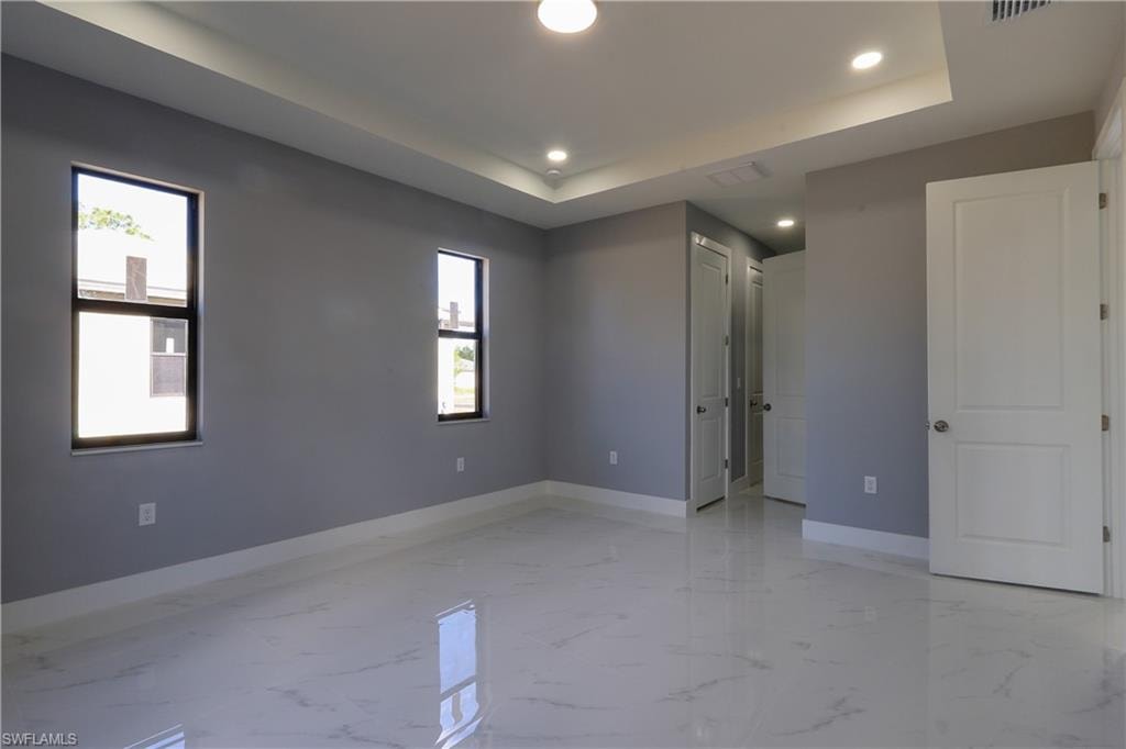 Unfurnished bedroom featuring recessed lighting, a tray ceiling, and light marble finish floors