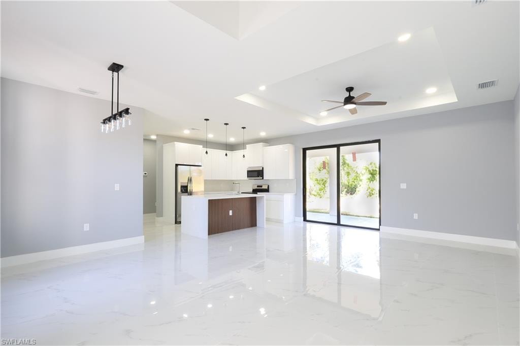 Kitchen featuring open floor plan, hanging light fixtures, recessed lighting, light marble finish flooring, and white cabinets