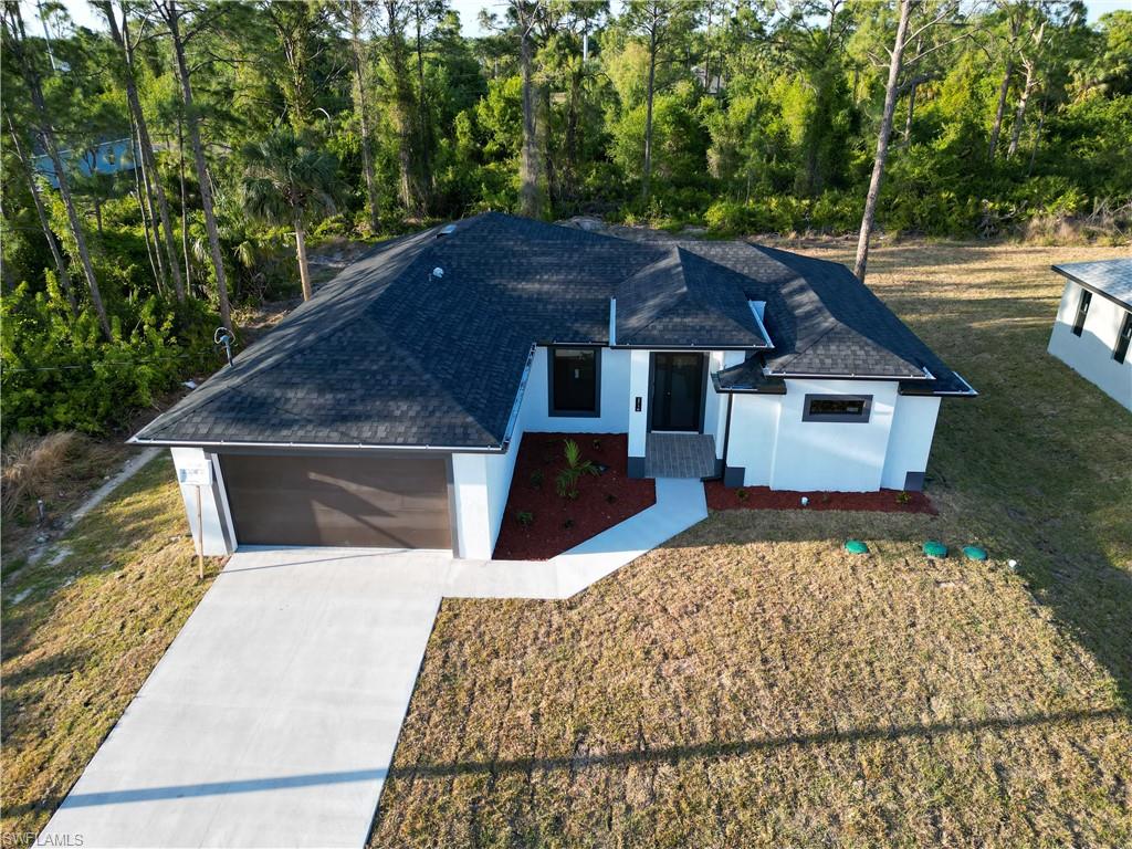 Ranch-style home featuring concrete driveway, a shingled roof, stucco siding, and a front yard