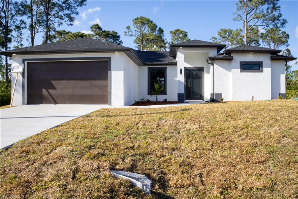 Prairie-style home featuring stucco siding, a front lawn, concrete driveway, and a garage
