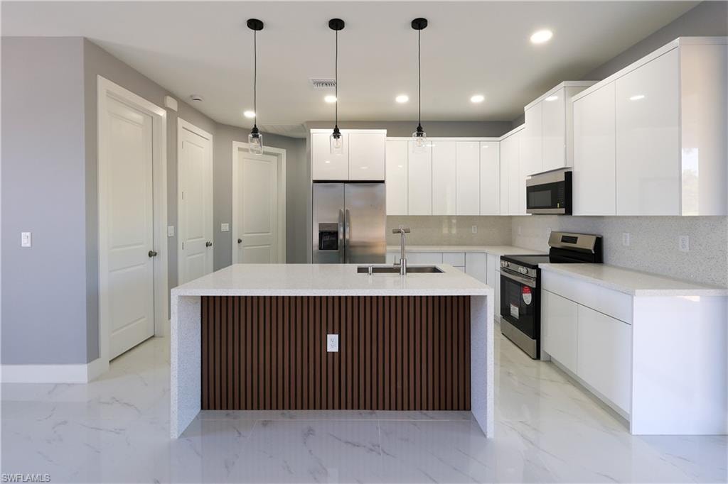 Kitchen with modern cabinets, appliances with stainless steel finishes, white cabinets, pendant lighting, and recessed lighting