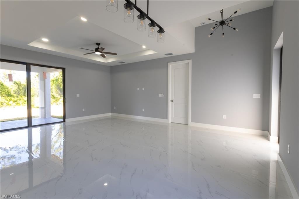 Spare room with a chandelier, light marble finish flooring, recessed lighting, ceiling fan, and a tray ceiling