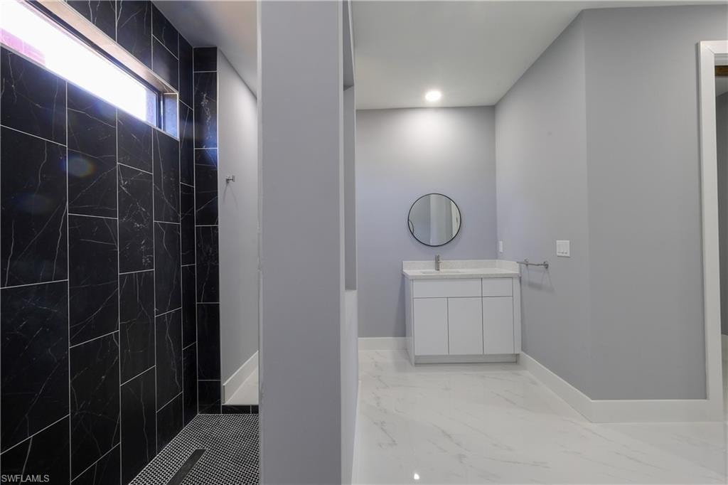 Full bath with light marble finish floors, a marble finish shower, and vanity