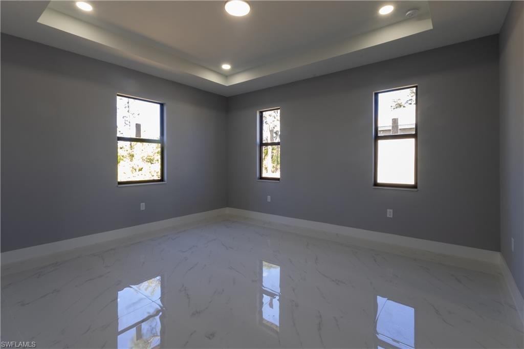 Empty room featuring marble tiled flooring, recessed lighting, and a raised ceiling