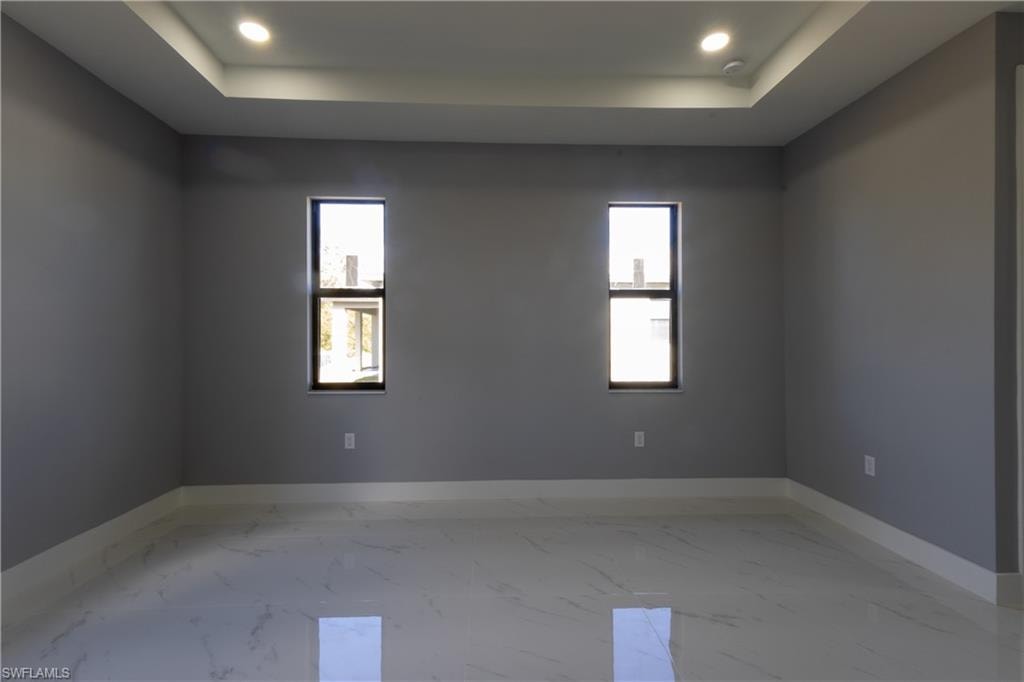 Unfurnished room featuring light marble finish flooring, a tray ceiling, and recessed lighting