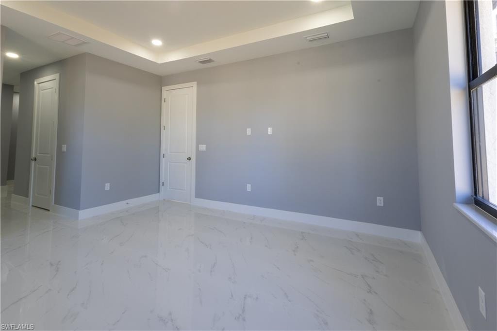 Empty room with recessed lighting, light marble finish floors, and a tray ceiling
