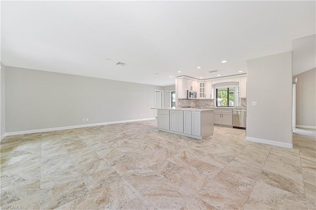 Spacious open concept living area featuring large format tile flooring and a kitchen with light-toned cabinetry, stainless steel appliances, and an island with bar seating
