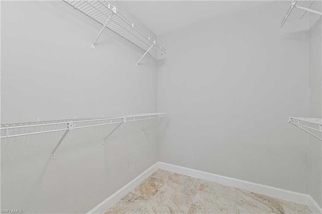 Walk-in closet featuring light gray walls, white wire shelving, and neutral-toned tile flooring