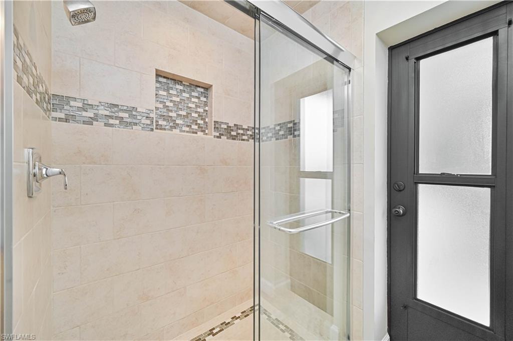 Shower with glass enclosure, beige tile walls, mosaic tile accent bands, built-in shower niche, and polished chrome fixtures