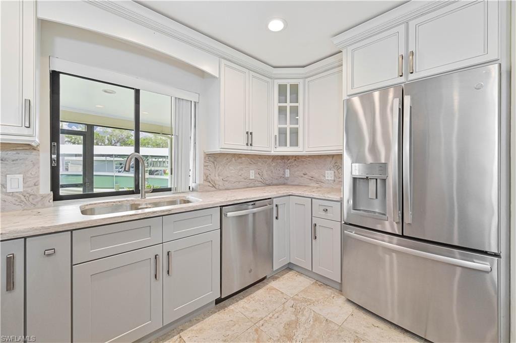 Modern kitchen featuring stainless steel appliances, light-toned countertops with a matching backsplash, white upper cabinetry, and contrasting light gray lower cabinetry