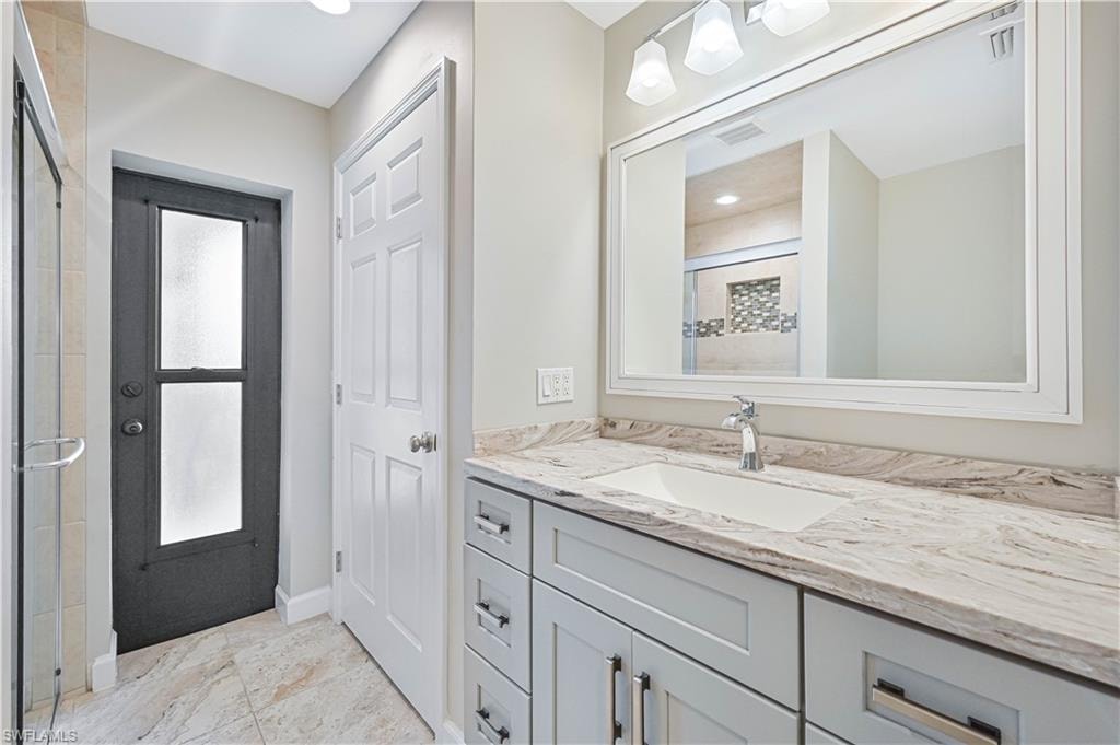 Bathroom featuring a light-toned vanity with an integrated sink, a framed mirror, and a three-light fixture