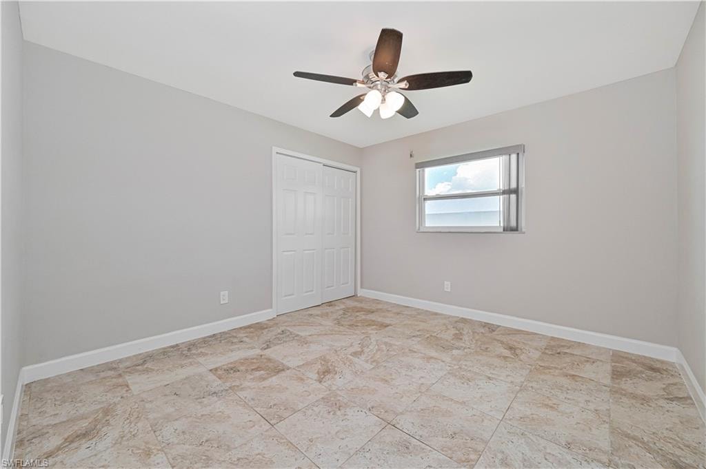 Spacious room featuring neutral wall tones, large format tile flooring, a window with horizontal blinds, a ceiling fan with integrated lighting, and a white bi-fold closet door