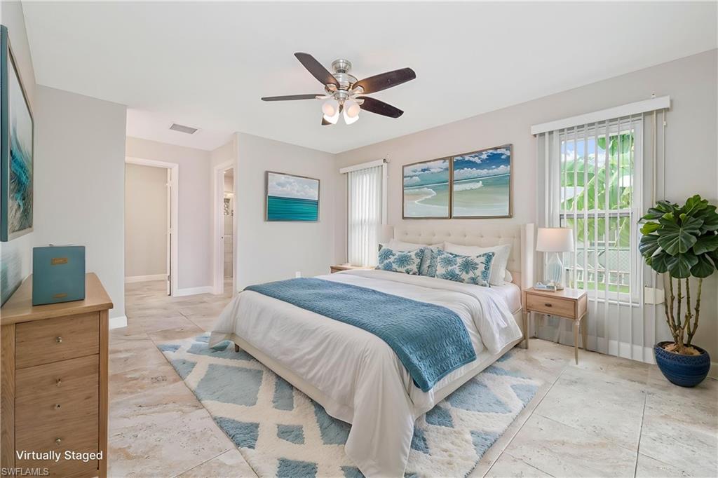 Spacious bedroom featuring light-toned tile flooring, a ceiling fan with integrated lighting, and multiple windows with vertical blinds