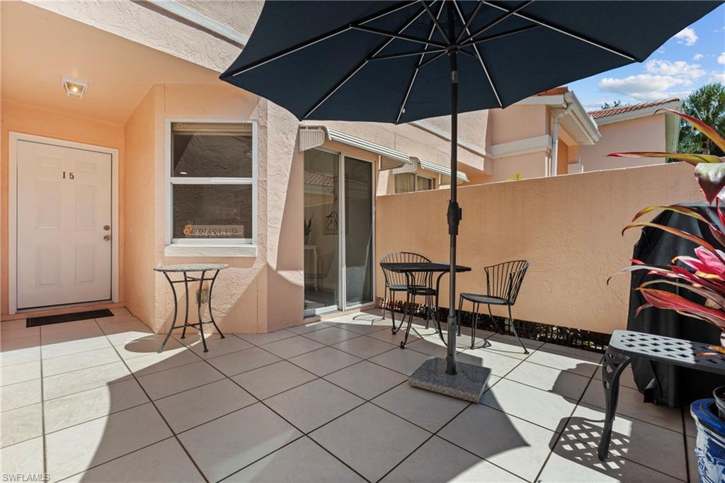 Spacious outdoor patio featuring light-toned square tile flooring, a solid privacy wall, and direct entry access