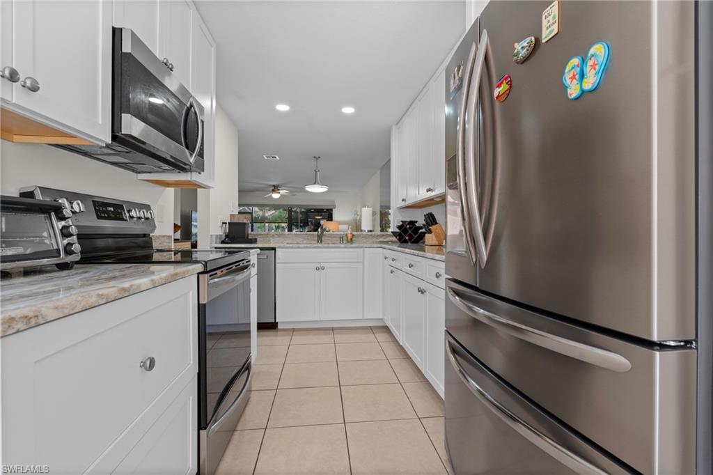 Modern kitchen with stainless steel appliances, white cabinetry, light-toned countertops, and tile flooring