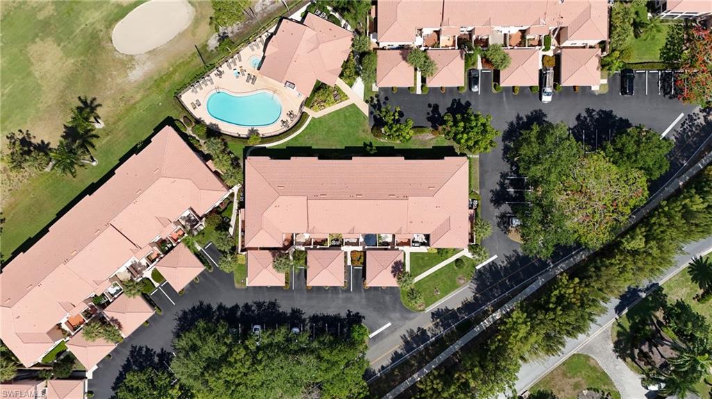 Community aerial showcasing multiple residential buildings with terracotta-style roofs, a central swimming pool with surrounding patio space, dedicated parking areas, and manicured green spaces