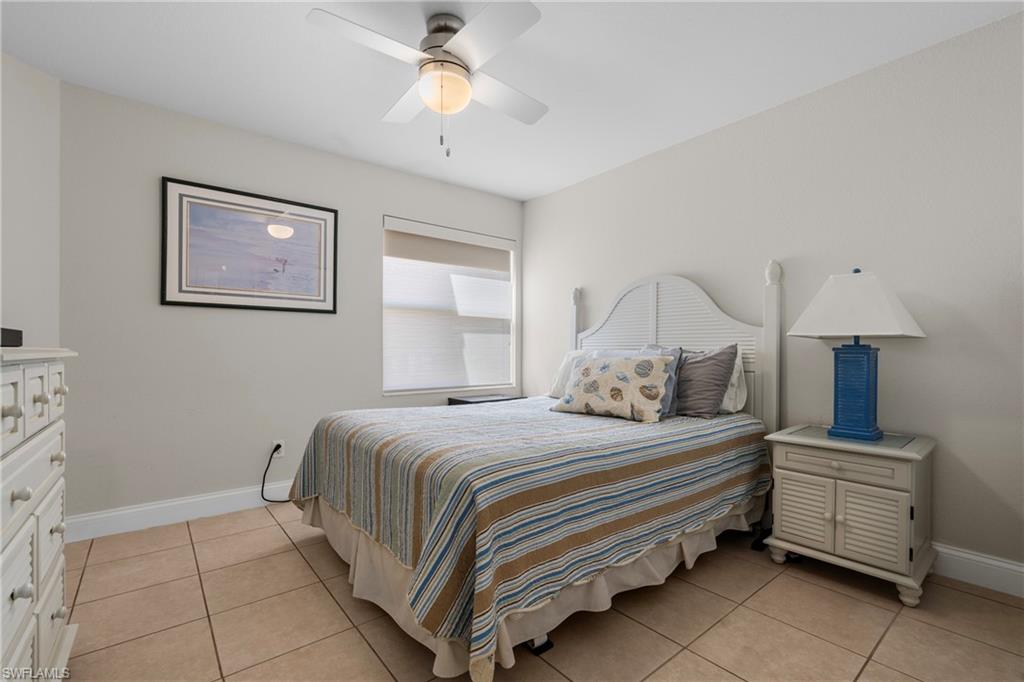 Bedroom featuring tile flooring, a window with roller shades, a ceiling fan with light fixture, and a louvered headboard